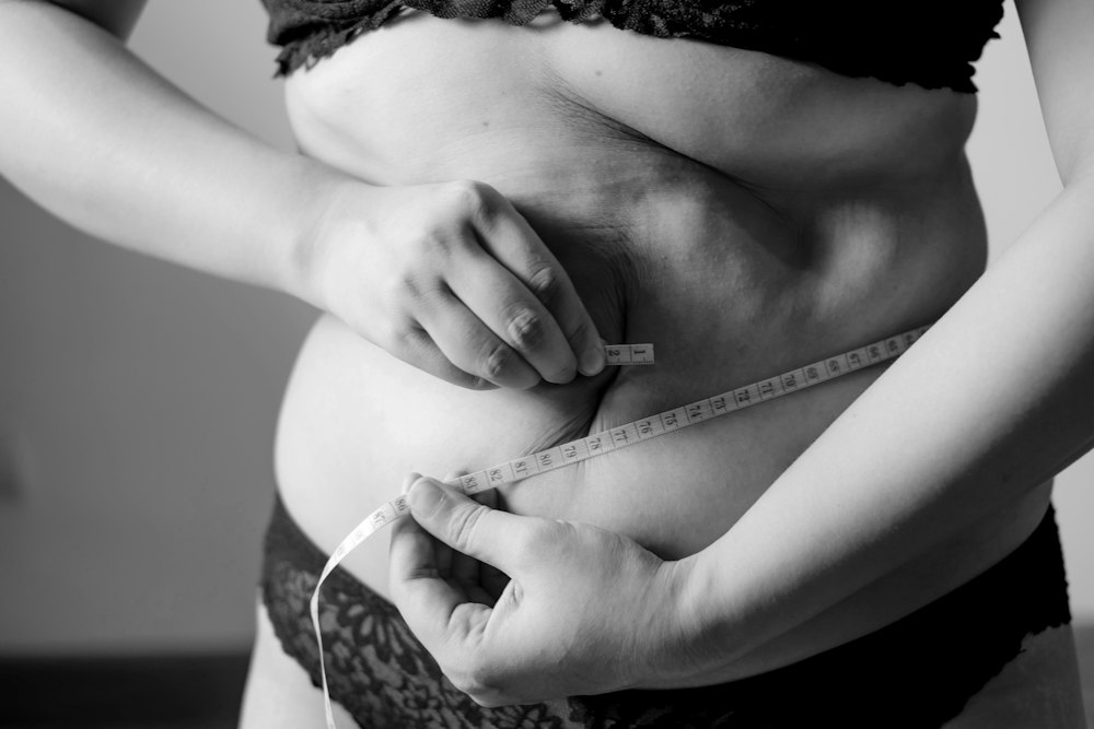 Mujer midiendo su cintura con una cinta métrica, en blanco y negro