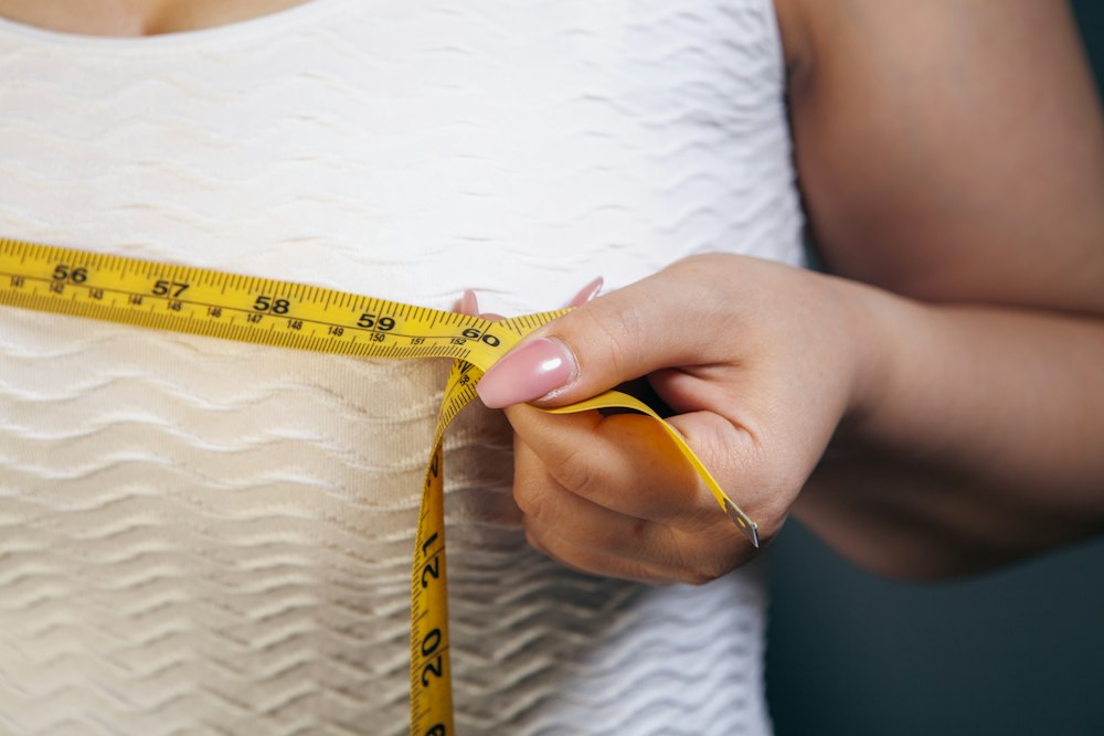Mujer con blusa blanca midiendo su busto con una cinta métrica